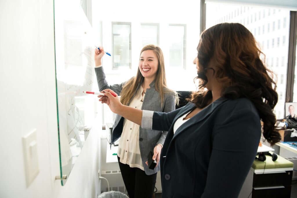 Deux femmes collaborant devant un tableau blanc lors d’un atelier bien-être et qualité de vie au travail animé par Marie Dias